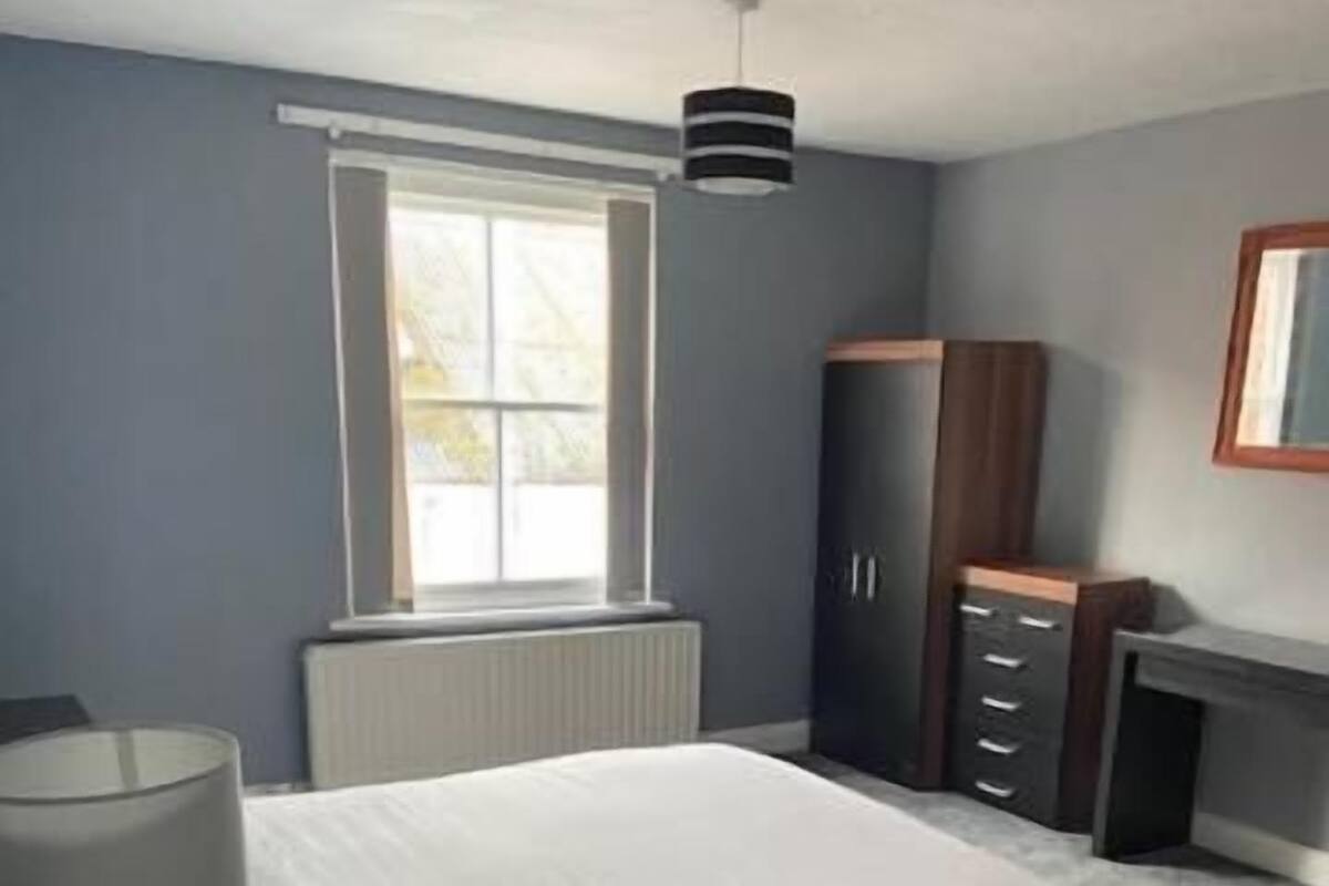 Ein Schlafzimmer mit Bett, Schminktisch, Lampe, Fenster und Heizkörper.