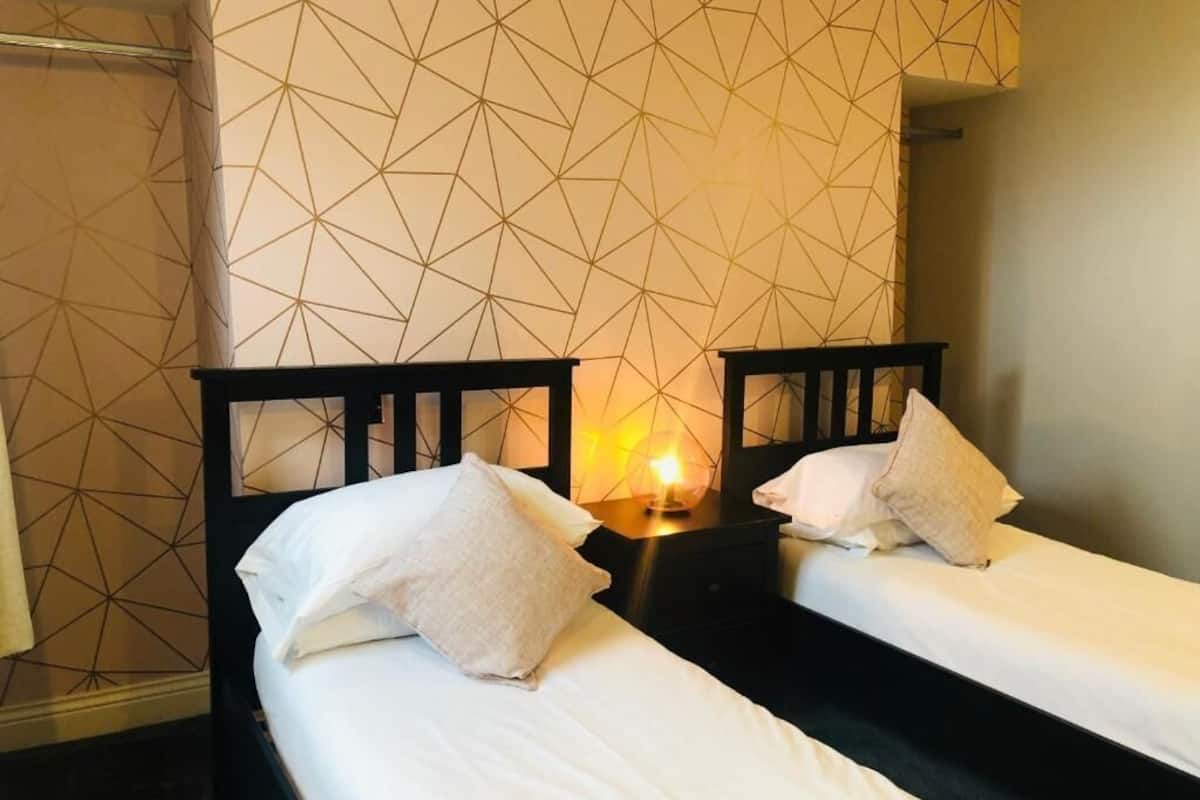 Ein Hotelzimmer mit zwei Einzelbetten, einem Nachttisch mit Lampe und einer Wand mit geometrischem Muster.