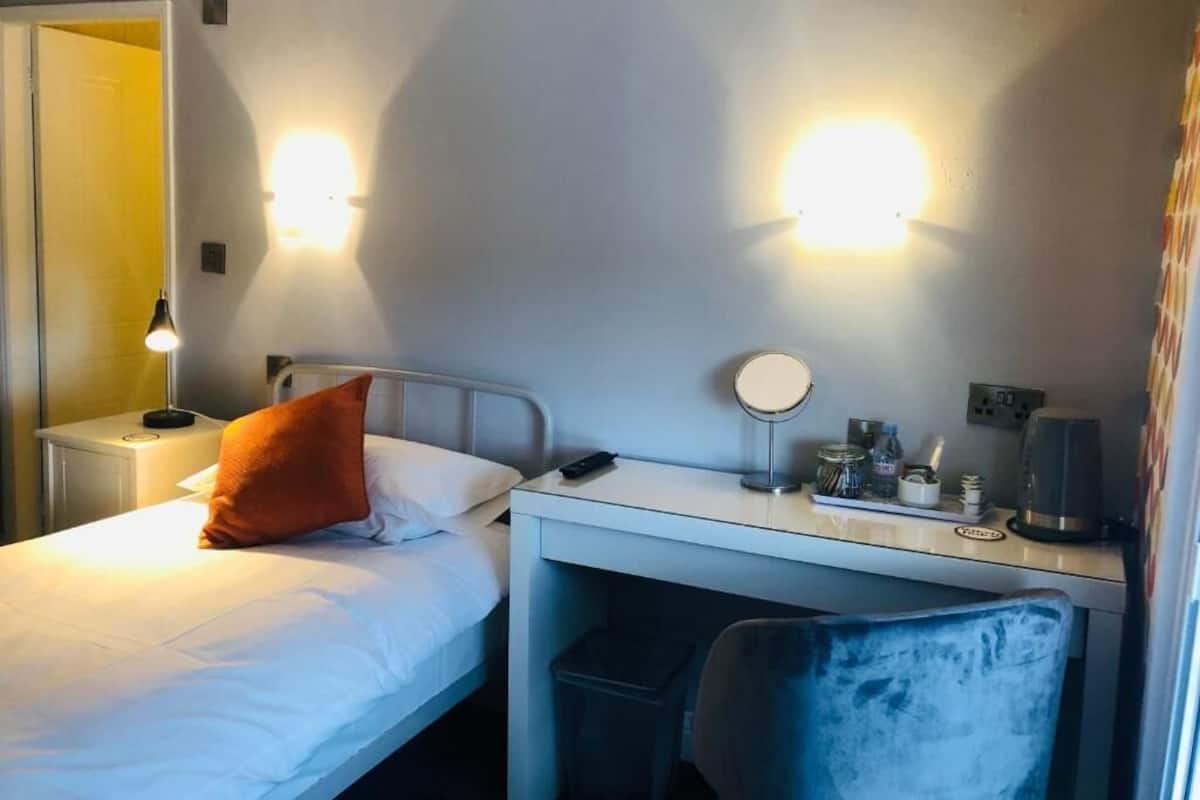Ein Hotelzimmer mit einem Bett, einem Schreibtisch mit Lampe, einem Spiegel und einem Sessel.