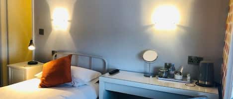 Una habitación de hotel con cama, escritorio con lámpara, espejo y silla.