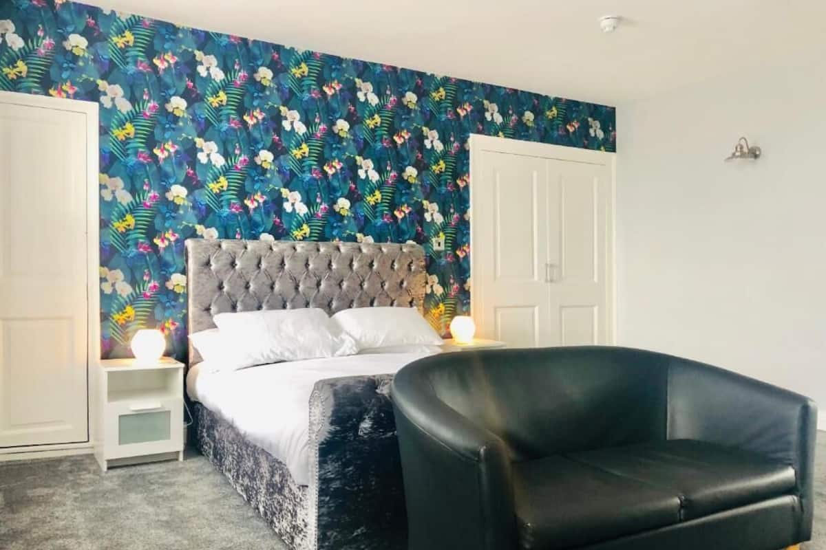 Ein Schlafzimmer mit einem gepolsterten Kopfteil, einem schwarzen Ledersessel und einer Wand mit floralem Muster.
