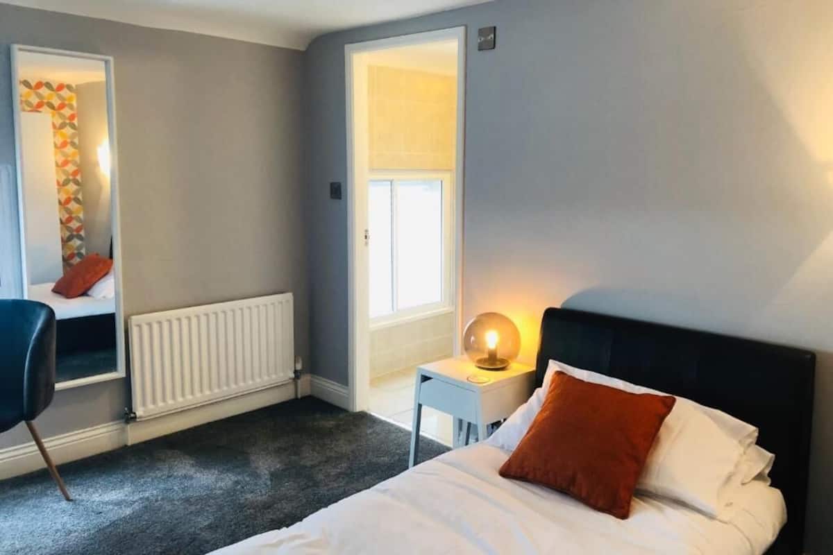Ein Schlafzimmer mit einem Bett, einem Nachttisch mit Lampe, einem Sessel, einer Heizung und einem Fenster.