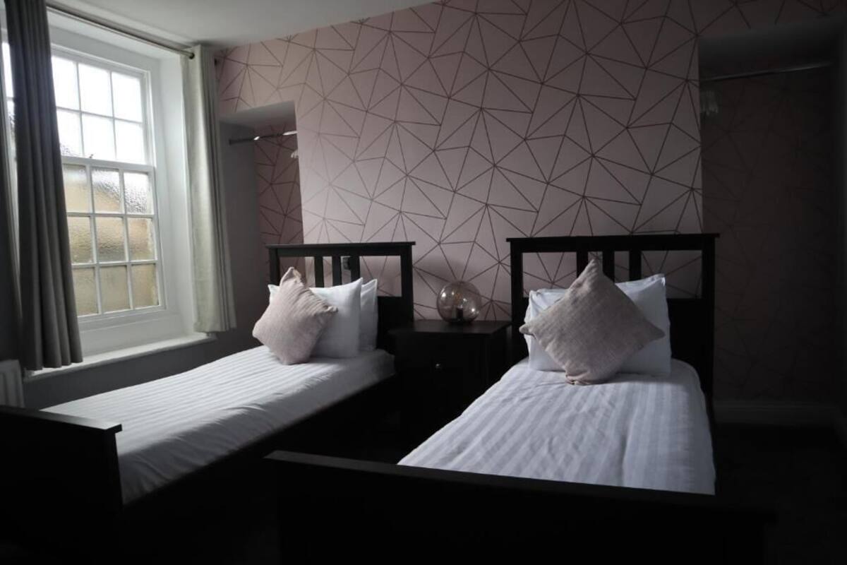 Ein Zimmer mit zwei Einzelbetten, einem fenster mit Vorhängen und einer Wand mit geometrischem Muster.