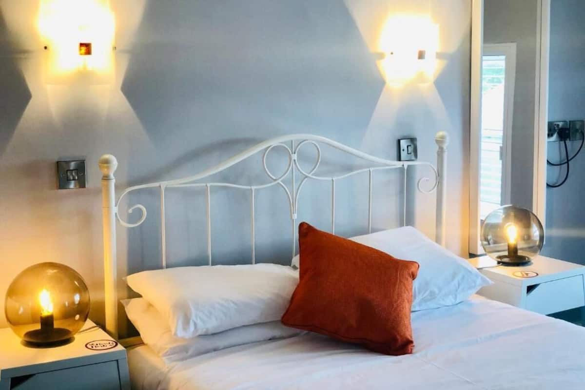 Ein Hotelzimmer mit einem weißen Metallbettgestell, weißer Bettwäsche, einem roten Kopfkissen und zwei Wandleuchten.