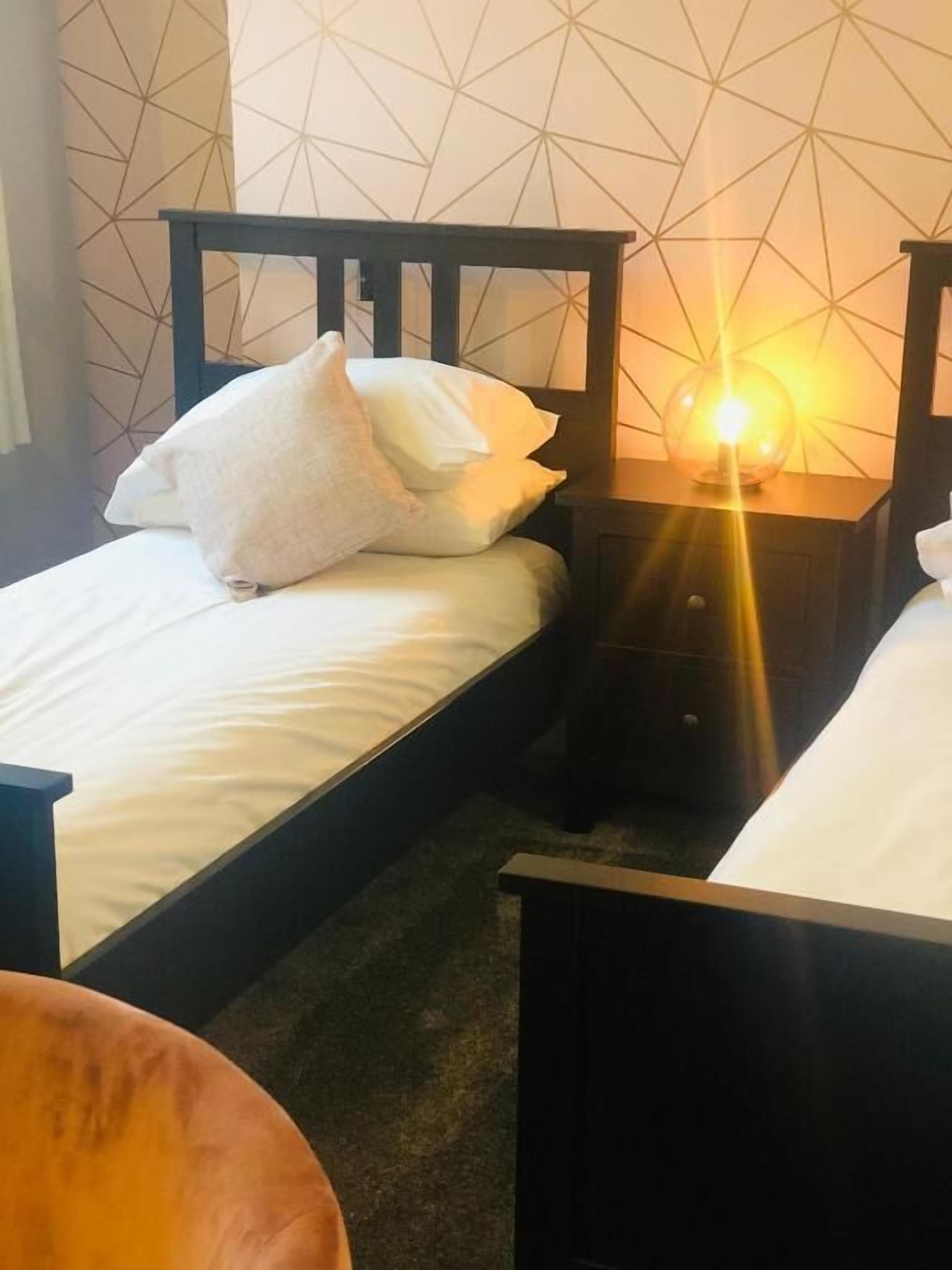 A hotel room with a bed, a nightstand with a lamp, and a geometric patterned wall.