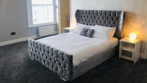 Makuuhuone, jossa on napitettulla päädyllä varustettu sänky, suuri ikkuna ja yöpöytä, jossa on lamppu.