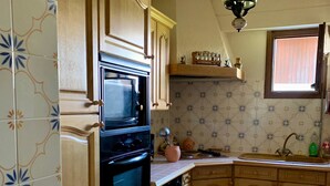 Een keuken met houten kastjes, een zwarte oven en een raam boven de gootsteen.