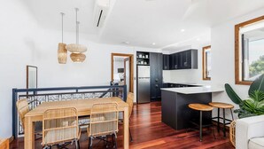 A modern kitchen with dark cabinets, a central island, and a dining area with wicker chairs.