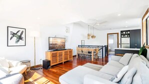 A modern living room with a sofa, TV, wooden cabinet, dining area, and kitchen.