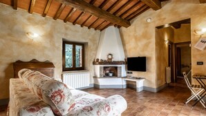 A cozy living room with a sofa, fireplace, TV, and wooden ceiling beams. - Holiday Home 'Colline' with Balcony and Wi-Fi (Radicofani)
