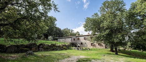 A stone building with a stone wall and a small bridge, surrounded by trees and grass.