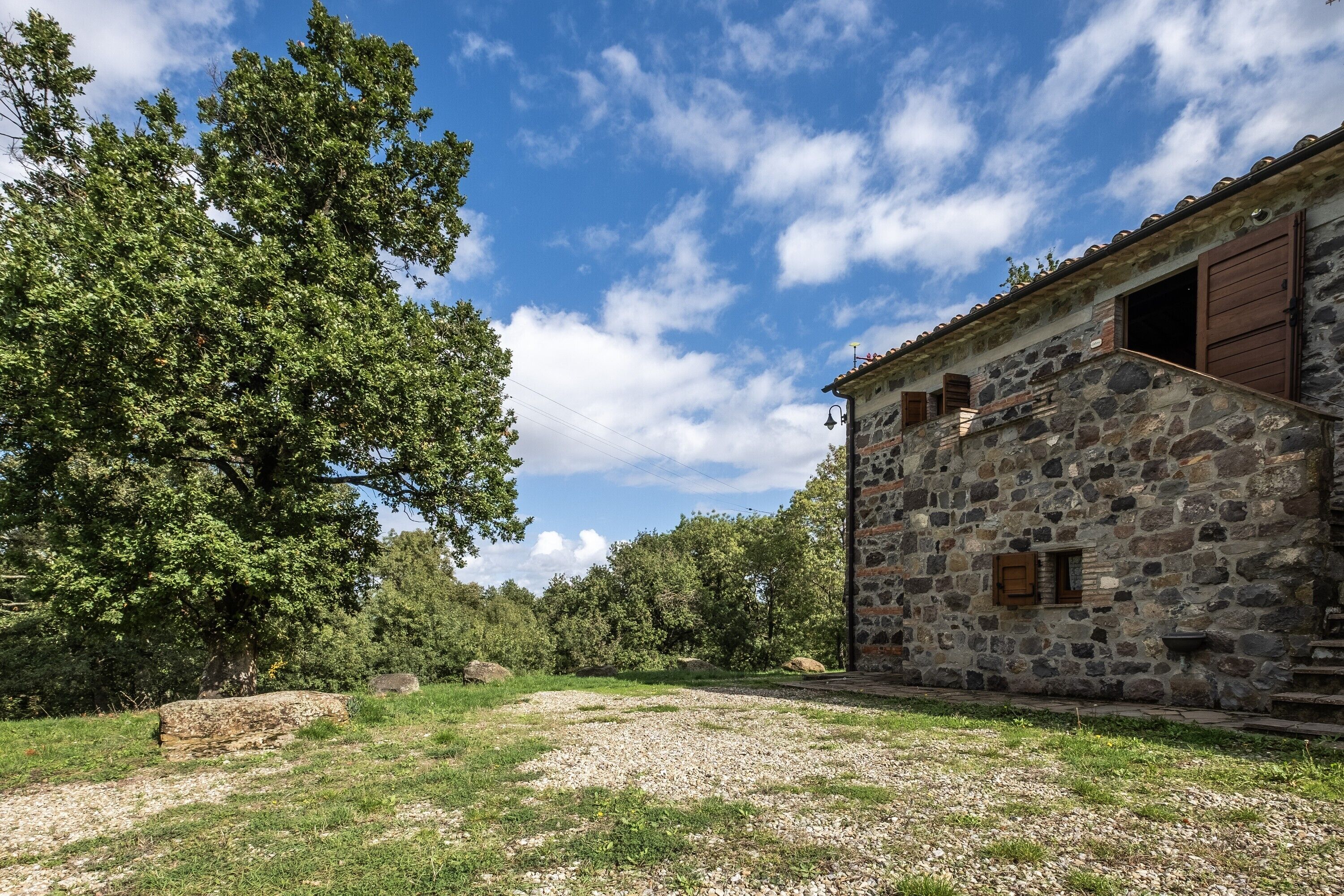 Un edificio de piedra con fachada rústica, un sendero de grava y un gran árbol en primer plano.