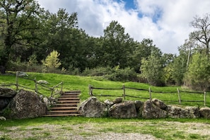 Eine Holztreppe führt einen grasbewachsenen Hügel hinauf, umgeben von einer Steinmauer und einem Holzzaun.