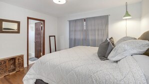 A bedroom with a large bed, a wooden cabinet, a mirror, and a door leading to another room. - Peaceful 3-bedroom house in quiet neighborhood with mature trees. (Wichita)