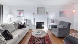 A living room with a white fireplace, a grey sofa, a grey armchair, and a coffee table. - Peaceful 3-bedroom house in quiet neighborhood with mature trees. (Wichita)