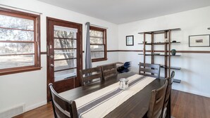 A dining area with a wooden table, chairs, a window, and a shelf with items. - Peaceful 3-bedroom house in quiet neighborhood with mature trees. (Wichita)