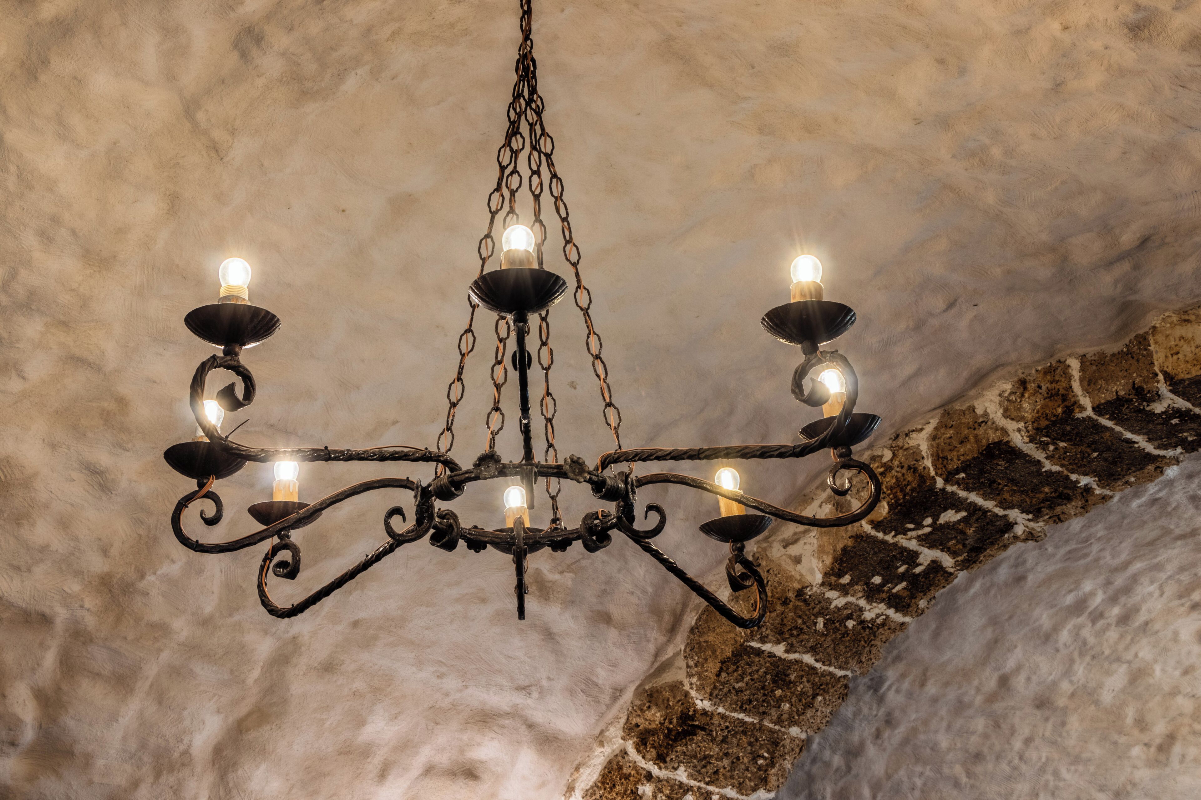 Um candelabro com várias luzes, suspenso por uma corrente em frente a uma parede texturizada.