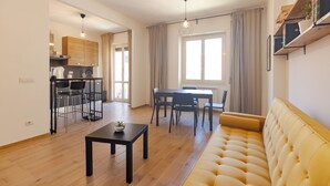 A modern living room with a yellow sofa, a dining table with chairs, a kitchen area, and a large window with curtains. - Moderno e comodo Metro Lucio Sestio (Rome)