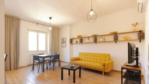 A living room with a yellow sofa, a dining table with chairs, a coffee machine, and shelves with decorative items. - Moderno e comodo Metro Lucio Sestio (Rome)