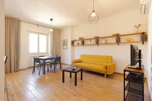 Un soggiorno con un divano giallo, un tavolo da pranzo con sedie, una macchina per caffè ed elementi decorativi su mensole.
