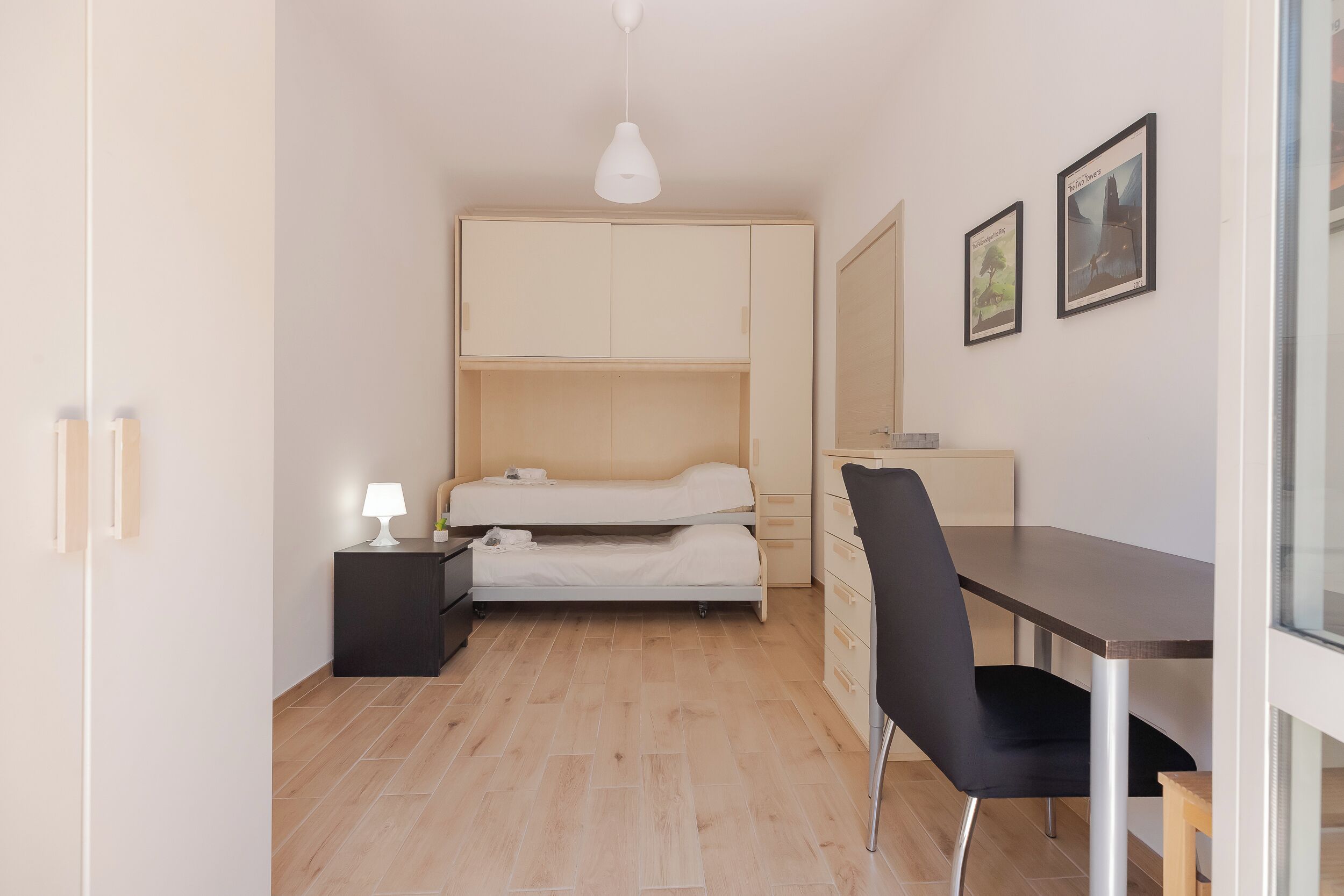 A compact room with a bunk bed, a desk, a chair, and a small table.