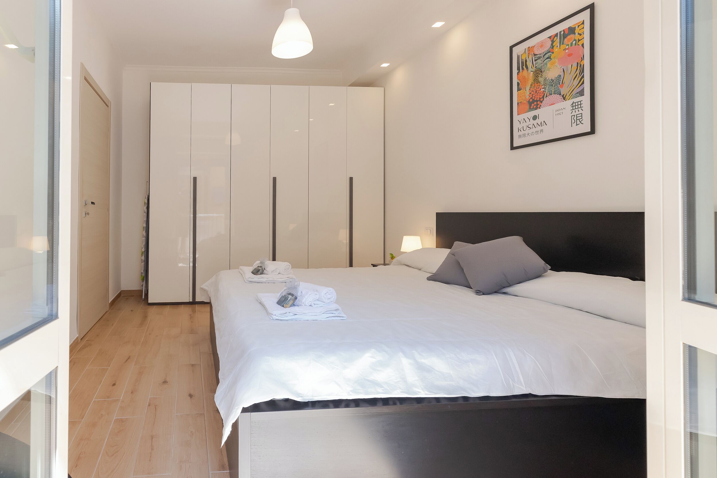 A hotel room with a bed, a wardrobe, a painting, and a window.