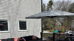 A covered outdoor deck with a sectional sofa, a grill, and a view of a residential neighborhood. - World Cup Stay in Easton! Elegant Suburban Escape Close to Boston Excitement (Easton)