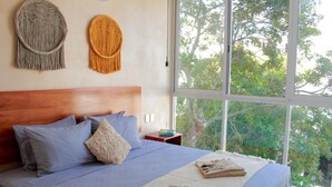 Un dormitori amb un llit gran, dues decoracions murals de borrons i vista a arbres a través d'una finestra ampla.