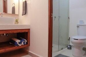 Une salle de bain avec un lavabo blanc, un meuble-lavabo en bois, une cabine de douche en verre et des toilettes.