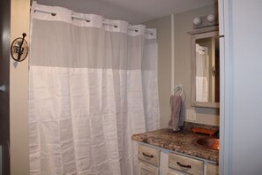 A bathroom with a shower curtain, a sink with a mirror, and a towel rack. - Otsego Lake Lodge - Your next destination! (Gaylord)