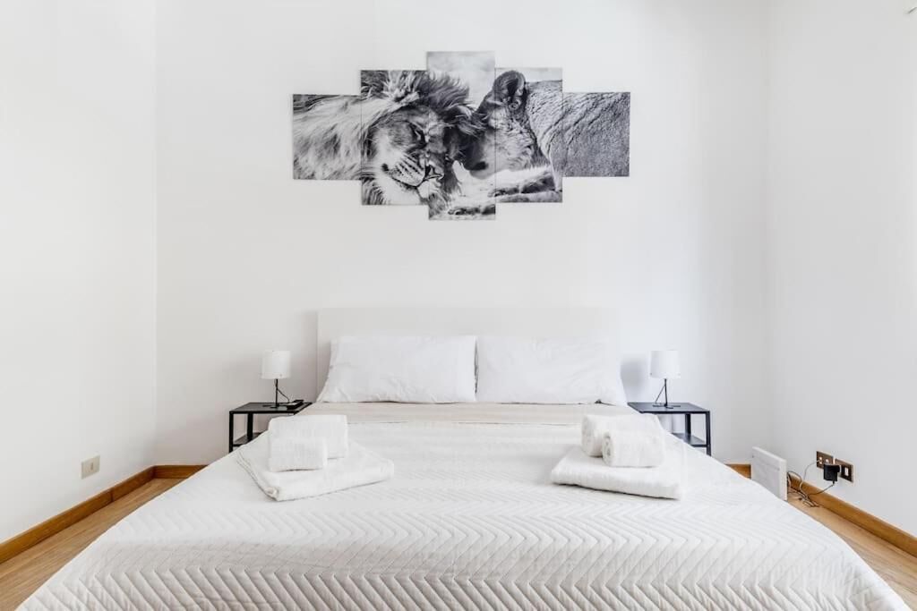 Ein modernes Schlafzimmer mit einem großen Bett, weißer Bettwäsche, zwei Nachttischen mit Lampen und einem Wandbild eines Löwen.