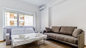 Een hotelkamer met een bed, een bank, een raam en een airconditioning.