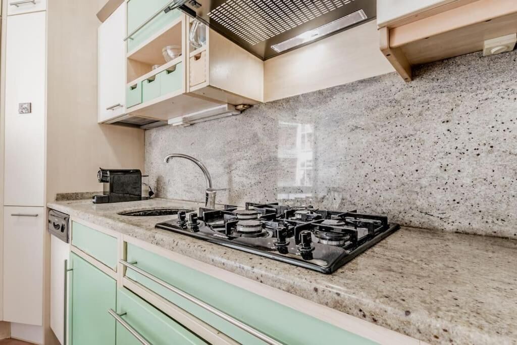 Una cucina con piano di lavoro in granito, fornelli a gas e mobili impiallacciati in verde chiaro.