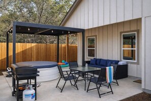 A backyard with a hot tub, a covered patio area, a seating arrangement, and a barbecue grill.
