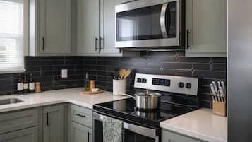 A modern kitchen with grey cabinets, a black tiled backsplash, stainless steel appliances, and a window with blinds.