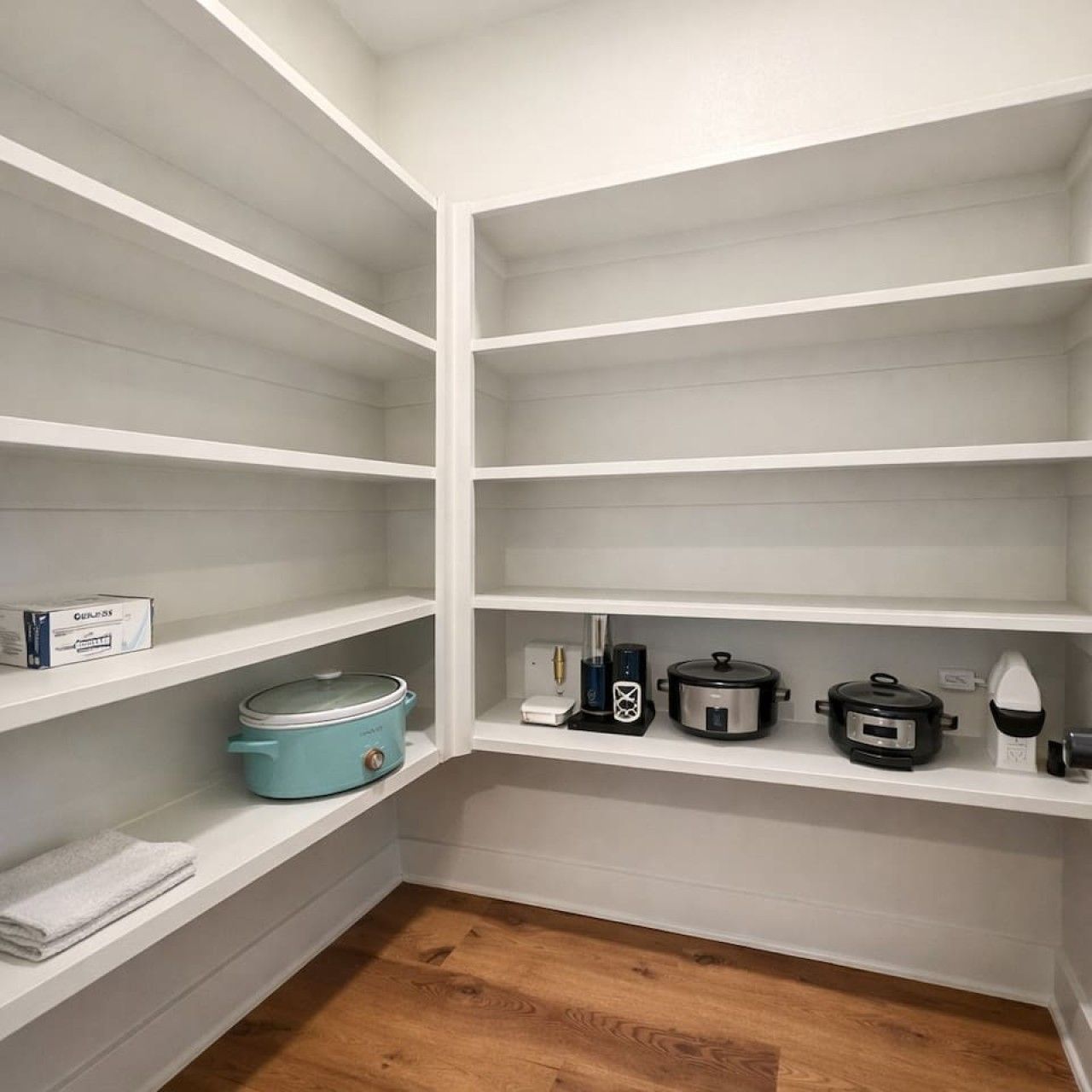 A kitchen with white shelves, a blue slow cooker, a coffee maker, and a kettle.