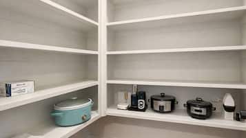 A kitchen with white shelves, a blue slow cooker, a coffee maker, and a kettle.