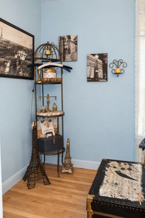 Une pièce avec un mur bleu, une étagère en métal de style vintage ornée d’objets décoratifs, un tableau encadré représentant la Tour Eiffel et une petite maquette de la Tour Eiffel posée sur le sol.