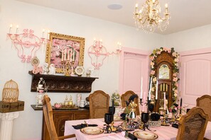 Une salle à manger avec une nappe rose, des lustres décoratifs et un décor d’époque.