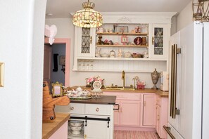 Een keuken met roze kastjes, een houten aanrechtblad en diverse decoratieve items op planken.