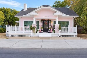 Een roze huis met een veranda, schoorsteen en een decoratieve krans.
