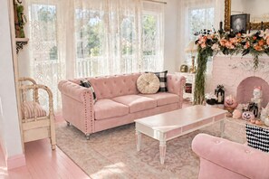 Een gezellige woonkamer met een roze bank, een witte salontafel en een open haard versierd met decoraties bijpassend bij het seizoen.