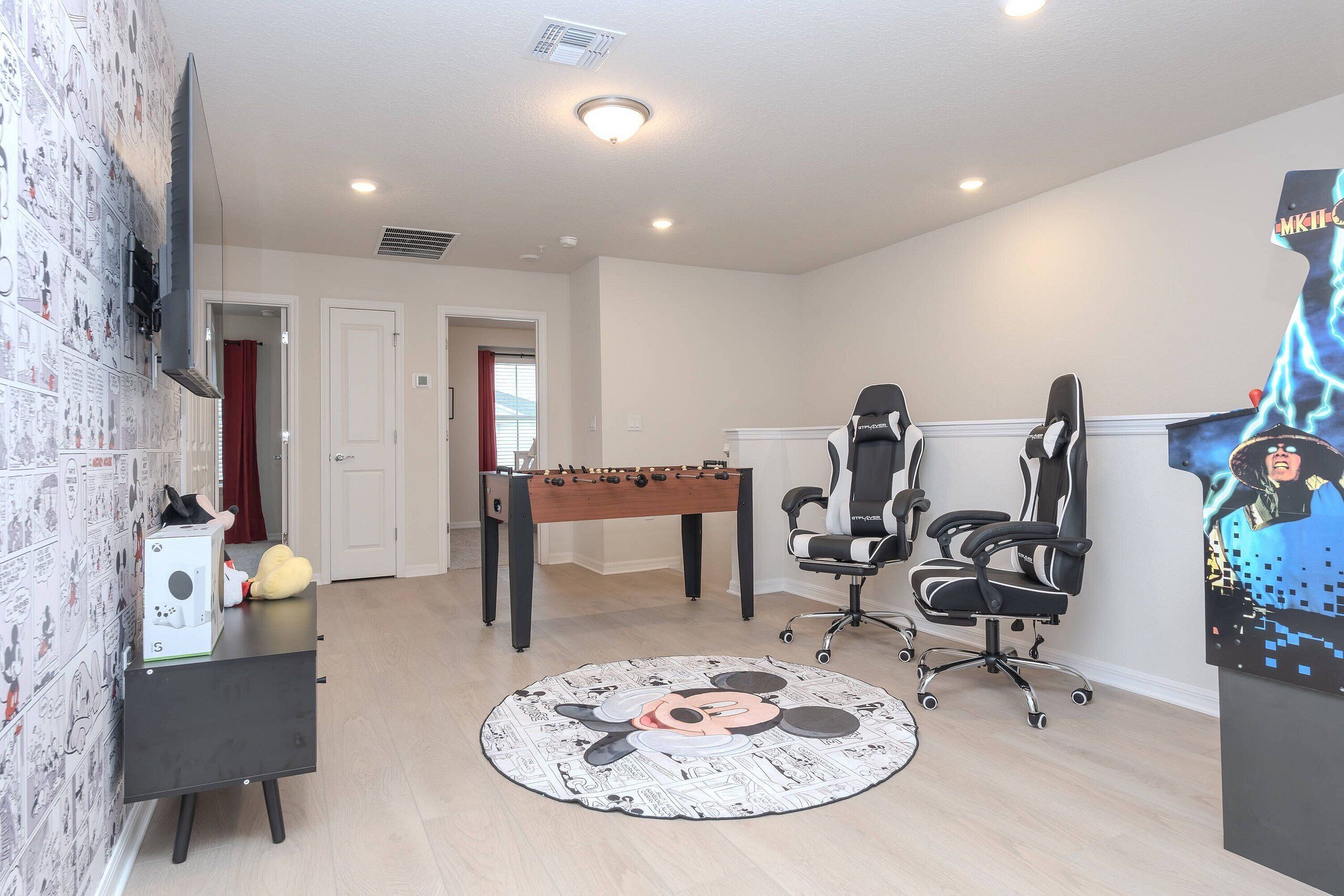A room with a foosball table, a gaming chair, a desk with a computer, and a wall-mounted TV.