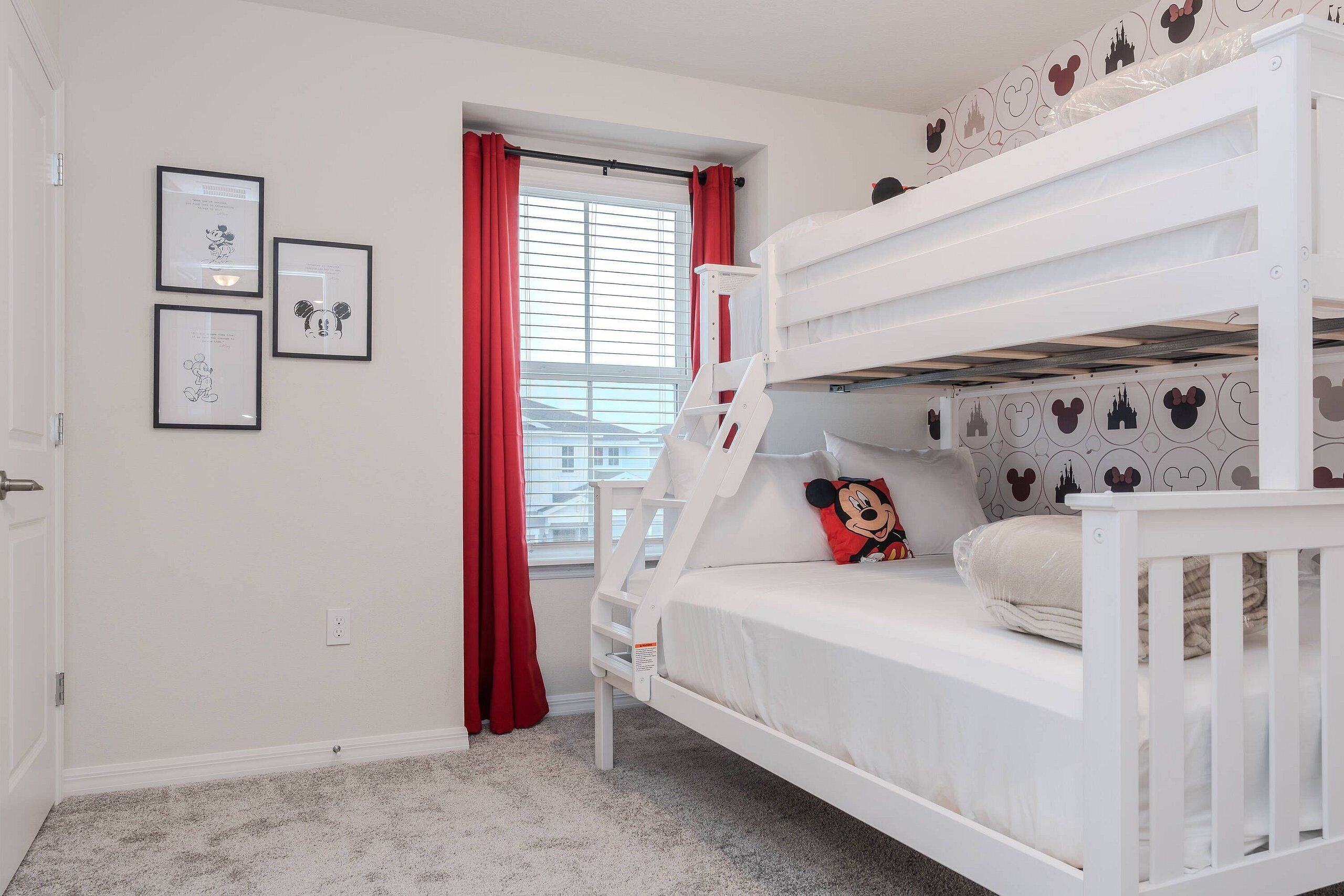 A bunk bed room with a window, red curtains, and framed pictures on the wall.