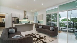 Una cocina moderna con armarios blancos, una isla central y un amplio ventanal con vistas a un balcón.