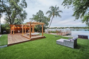 Een houten terras met een pergola, zitmeubels en uitzicht op een meer.