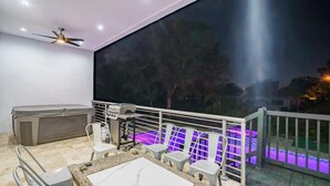 Un balcón con piscina, ventilador de techo, parilla y una mesa con sillas.