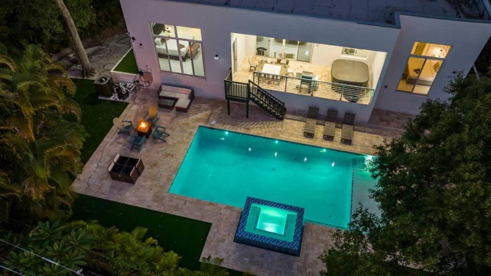 A modern house with a large swimming pool, a covered patio, and a well-lit interior.