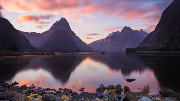 Un lago tranquilo con montañas reflejadas en el agua, rodeado de costas rocosas.