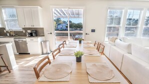 Una cucina moderna con mobili bianchi, una lavastoviglie e una macchina da caffè. C'è un tavolo da pranzo con sottopiatti e sedie, e un divano bianco nella zona living.